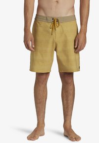 Shorts de bain à carreaux jaunes en tissu doux, avec une taille élastique et un système de fermeture par cordon. Comprend des poches latérales et un design léger.