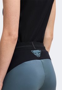 Gros plan d'une personne portant des leggings de sport noirs et bleus avec un logo stylisé de visage d'animal sur la ceinture arrière.
