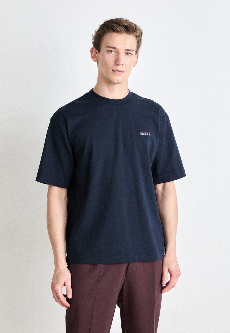 Μπλε ναυτικού βαμβακερό μπλουζάκι με κοντά μανίκια και λαιμόκοψη τύπου crew. Περιλαμβάνει ένα μικρό λογότυπο "BOSS" στο στήθος. Εύκολη υφή, χαλαρή εφαρμογή.