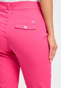 Roze broek met een gladde textuur, voorzien van een achterzak met een knoopsluiting en een metalen accent op de zak.