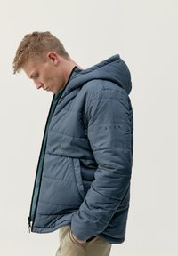 Mornarsko modra puhasta jakna s kapuco, z oblazinjenim dizajnom, zadrgo in stranskimi žepi. Narejena iz gladkega, lahkega materiala.