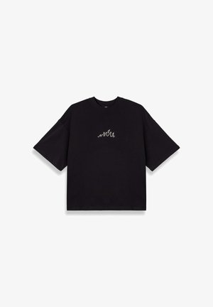 Schwarzes, oversized T-Shirt aus Baumwolle mit kurzen Ärmeln. Verfügt über ein kleines, weißes Wellenmotiv, das auf der Brust gestickt ist. Schlicht und modern geschnitten.