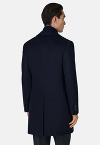 Abrigo de lana en color navy con solapa muesca, abertura central y botones en los puños. Textura suave con un corte ajustado.