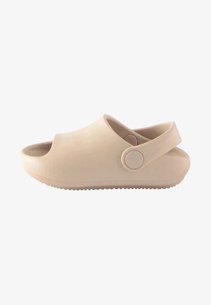 Beige Gummischlappen mit offener Zehe und Rückenriemen, mit glatter Textur, runder Form und einem runden Knopfakzent am Riemen.