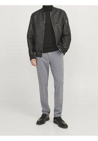 Black leather bomber jacket over a black turtleneck, paired with light gray tailored pants and black lace-up shoes.