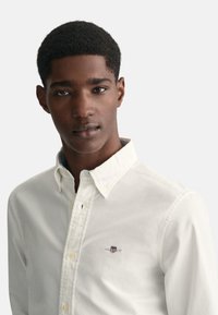 Chemise blanche à boutons en coton avec col, dotée d'un logo brodé. Texture lisse et coupe classique.