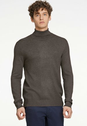 Mørkebrun turtleneck sweater lavet af blødt strikstof, med lange ærmer og tætsiddende manchetter, kombineret med marineblå bukser.