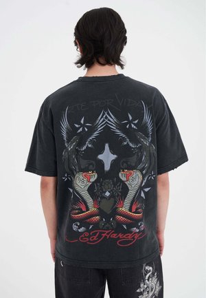 Černé oversized tričko s grafickým motivem dvou hadů a ptáků, s nápisem "Arte Por Vida" a "Ed Hardy" v tučně červené barvě. Ošuntělé okraje.