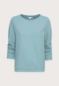 Sweat-shirt bleu clair texturé avec un col rond et des manches longues légèrement froncées. Présente des poignets et un ourlet côtelés.