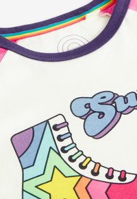 Kortærmet skjorte med et multicolor skate-design med stjernemønstre, en hvid bund og en lilla krave.