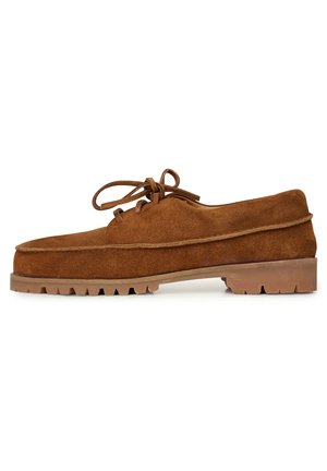 Scarpa in suede marrone con lacci e suola spessa, dotata di punta arrotondata e suola testurizzata per la trazione. Semplici cuciture decorative lungo i bordi.