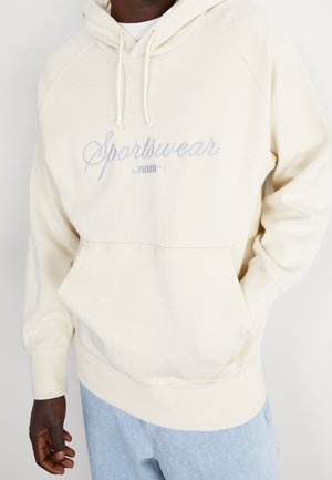 Sweatshirt à capuche crème avec "Sportswear by PUMA" brodé en bleu clair. Dispose de poignets côtelés, d'une poche kangourou et d'une texture douce.