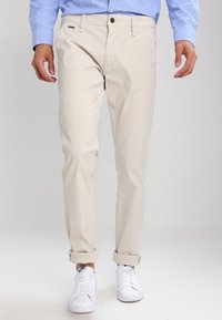 Pantaloni in cotone beige a vestibilità slim, con chiusura a bottone, orli arrotolati e tasche laterali, abbinati a sneaker bianche.