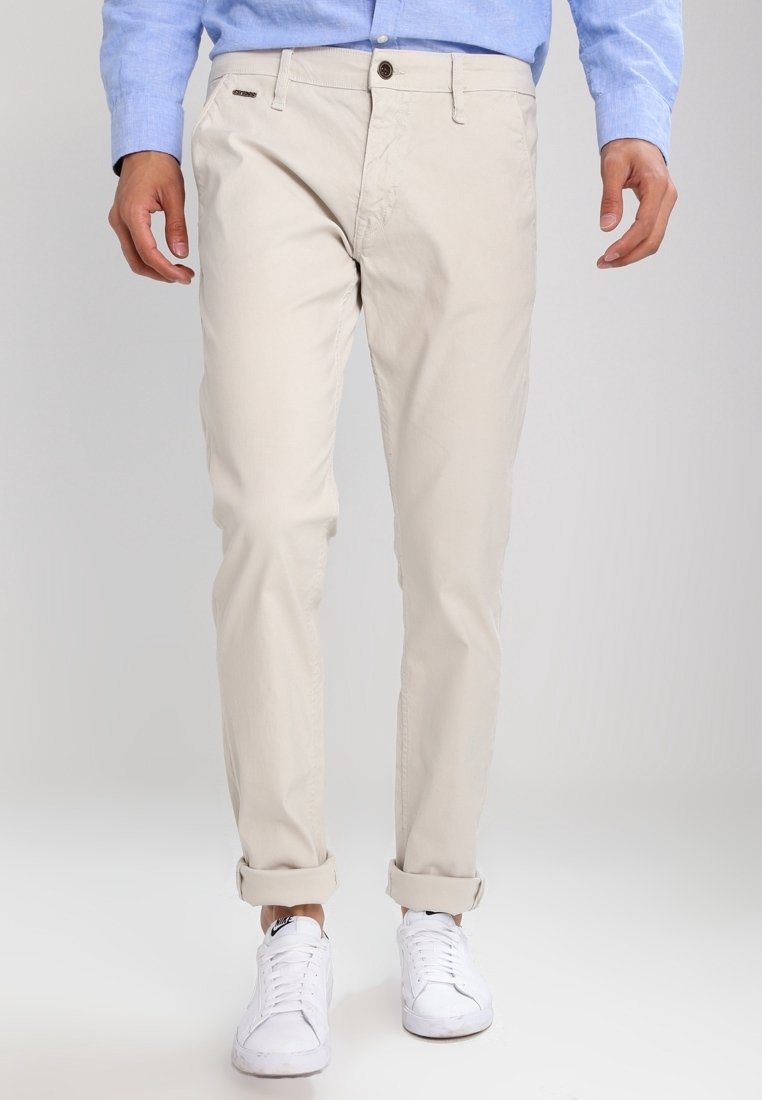 Beige katoenen broek met een slim fit, voorzien van een knoopsluiting, opgerolde manchetten en zijzakken, gecombineerd met witte sneakers.