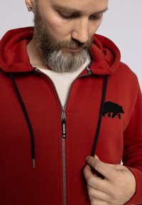 Felpa rossa con zip realizzata in tessuto morbido. Caratterizzata da una silhouette di orso nero e da cordini neri a contrasto. Zip con etichetta del marchio.