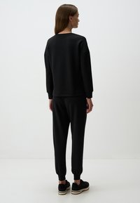 Felpa nera con collo a giro e spalle cadute, abbinata a pantaloni della tuta a sigaretta coordinati. Il materiale sembra morbido e confortevole.