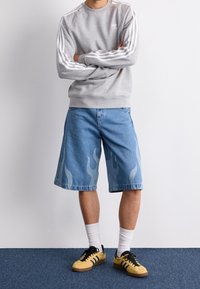 Grå sweatshirt med vita ärmstripes, blå denim-shorts med ljusa flamdekorer, och gula sneakers med svarta detaljer.