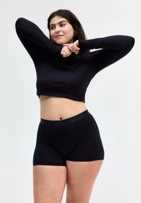 Schwarzes langärmliges Cropped-Top, kombiniert mit schwarzen hochgeschnittenen Shorts. Beide haben eine glatte Textur und ein figurbetontes Design. Schlichte, minimalistische Akzente.