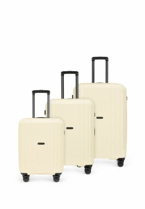 Three cream-colored hard-shell suitcases of small, medium, and large sizes with black telescoping handles and four wheels each.
