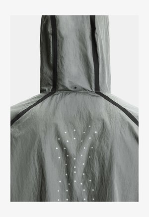 Veste grise à capuche avec des rayures verticales noires et un motif de petits points blancs formant un Y dans le dos.