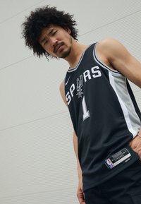 Juodas krepšinio marškinėliai su baltais ir pilkais akcentais, su užrašu "SPURS", numeriu "1" ir Nike logotipu. Tekstūruota medžiaga su šoniniais etiketės detalėmis.