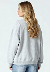 Harmaa huppari rentoa istuvuutta tarjoavalla leikkauksella, ribbaavat hihansuut ja helma. Pehmeä rakenne, leveät hihat ja minimalistinen muotoilu.