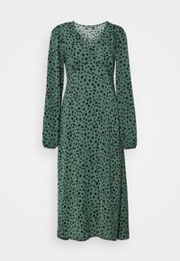 Grünes Langarmkleid mit V-Ausschnitt, das ein Muster aus schwarzen Punkten aufweist, eine taillierte Taille und einen fließenden Rock hat. Glatte Stofftextur.