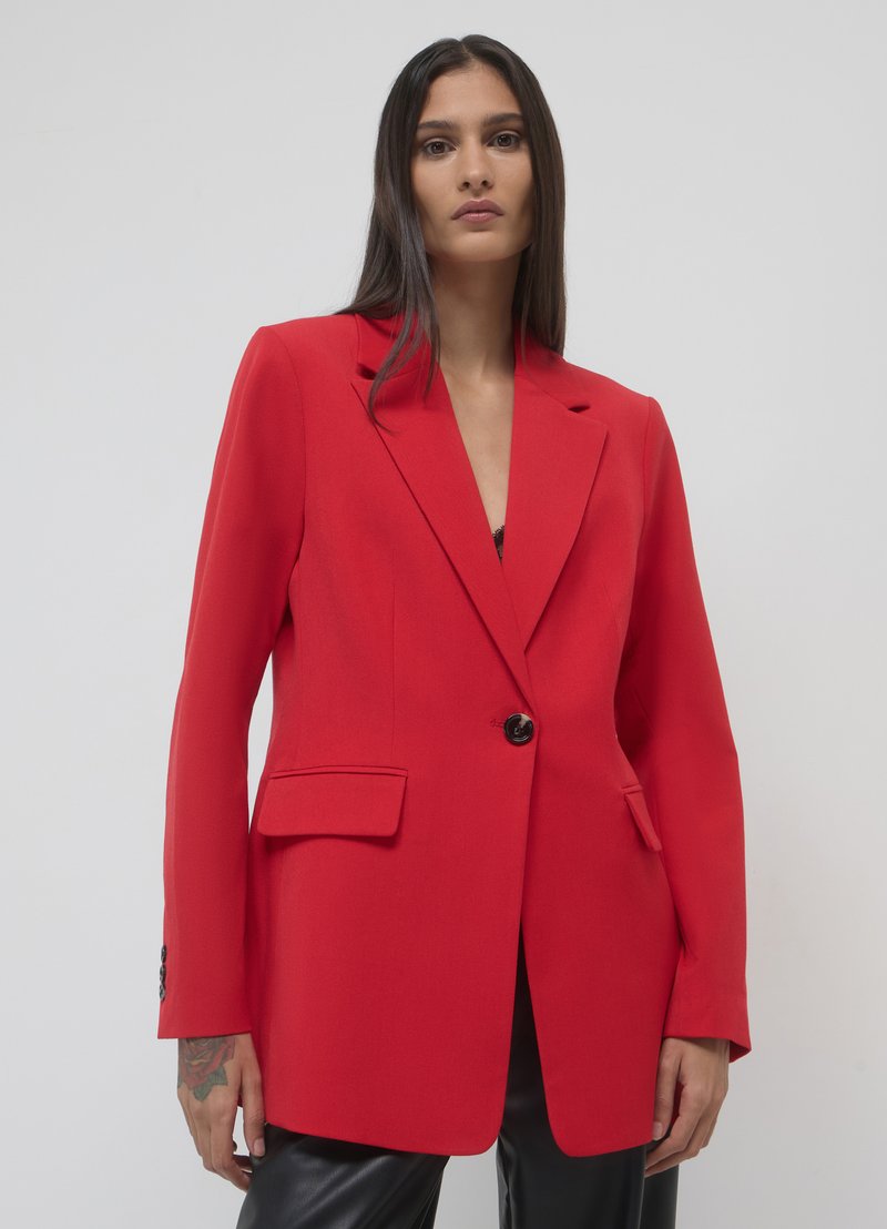 Blazer ajusté rouge avec un bouton unique à l'avant, revers à cran et deux poches avant. Il est doté de manches longues et de épaules structurées.