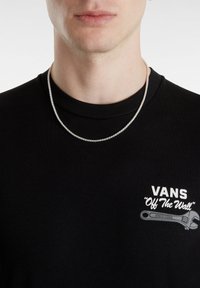 Collar de cadena de plata llevado sobre una camiseta negra de cuello redondo con un logotipo y un gráfico de llave inglesa, mostrando una textura metálica suave.
