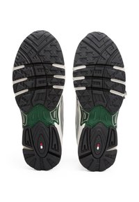 Semelles de chaussures de sport en caoutchouc noir avec un motif de crantage texturé, présentant des accents verts et une semelle intermédiaire blanche.
