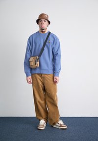 Blå sweatshirt, brune corduroybukser, brun bucket hat og crossbody-taske. Sko: hvide med brune detaljer. Enkel design, afslappet pasform.