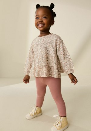 Light floral-patterned top with long sleeves, tiered ruffle, paired with ribbed pink leggings and light-colored high-top sneakers.