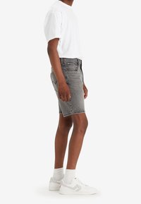 Shorts de denim gris con un corte clásico, que presentan un bolsillo frontal, bolsillos traseros y un desvanecimiento sutil, combinados con una camiseta blanca lisa y zapatillas.