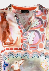 Bunte gemusterte Bluse mit V-Ausschnitt, kurzen Ärmeln und Darstellungen von Hunden in Verbindung mit verschiedenen abstrakten Formen in sanften Tönen.