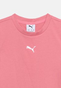 Κοντινό πλάνο στον ριμπ ύφασμα γιακά ροζ πουκάμισου με το λευκό λογότυπο Puma κεντημένο κάτω από τη γραμμή του λαιμού και ετικέτα μεγέθους στο εσωτερικό του γιακά.