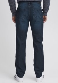 Jeans in denim blu scuro, design a gamba dritta, con due tasche posteriori caratterizzate da un sottile motivo a zigzag, indossati con sneakers bianche.