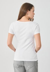 Balts īsām piedurknēm T-krekls ar apaļu dekoltē, mīksta tekstūra un pieguļošs dizains, kombinēts ar pelēkiem džinsiem un akcentētiem šuvumiem uz kabatām.