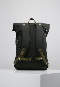 Czarny plecak z wyściełanymi, regulowanymi zielonymi ramiączkami, uchwytem u góry oraz boczną kieszenią na zamek dla łatwego dostępu. Teksturowany materiał z usztywnioną konstrukcją.