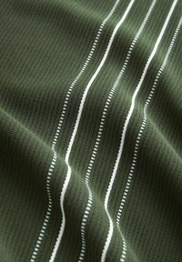 Tejido de ribetes verde oscuro con rayas blancas verticales. La textura es sutil y las rayas varían en ancho, creando un patrón rítmico.