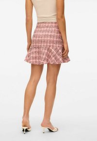 Jupe évasée rose avec un motif texturé à carreaux, détail à la taille et ourlet froncé. Assortie à des mules à talons ouverts beiges.