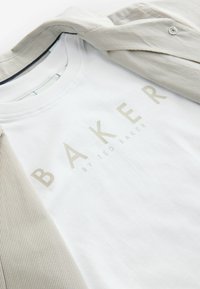 Weißes Baumwoll-T-Shirt mit der Aufschrift "BAKER" in hellgold, kombiniert mit einem hell gestreiften Hemd mit Knöpfen. Geschmeidige Textur, lässiges Design.