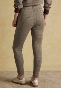 Bēšas krāsas houndstooth raksta legingi ar augstu vidukļa daļu, gluda tekstūra un piegulošs siluets. Kombinēti ar gaišām kedām.