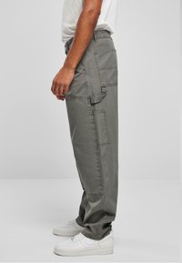 Pantalones cargo de color gris claro con múltiples bolsillos, un ajuste relajado y una tela de mezcla de algodón resistente, combinados con zapatillas blancas.