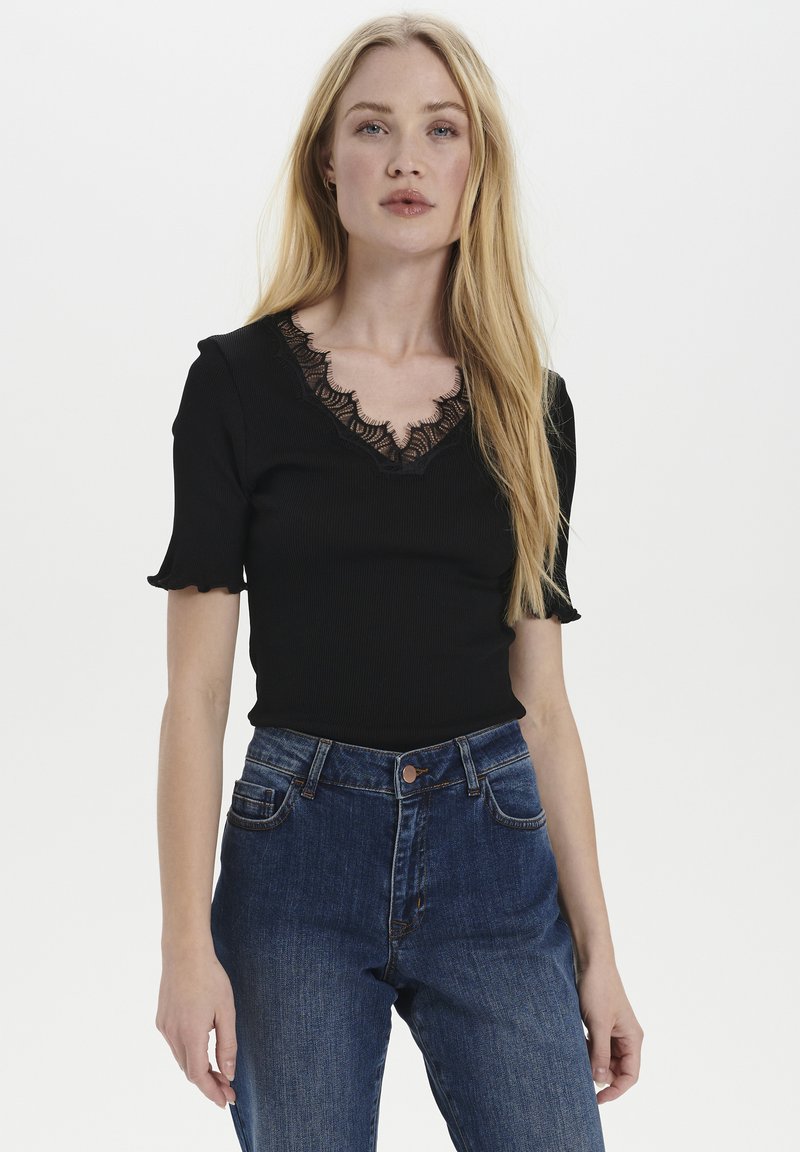 Top nero a coste con scollatura in pizzo a onde e maniche corte a volant. Abbinato a jeans in denim blu a vita alta.