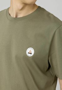T-shirt en coton vert olive avec un patch circulaire "Prenez une pause" avec des graphiques de flammes, col ras du cou classique et coupe standard.