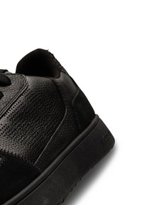 Crne tenisice s teksturiranim kožnim gornjištem, glatkim kontrastnim detaljima, okruglim vrhom i gumenim potplatom s vidljivim uzorkom.