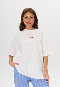 Witte oversized t-shirt van katoen, met rode "MIRONS" tekst op de voorkant. Korte mouwen en een relaxte pasvorm, gecombineerd met blauw gestreepte broek.