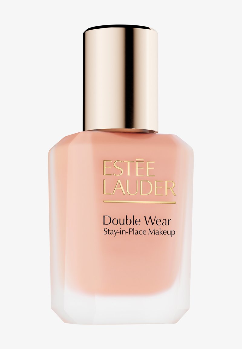 Fond de teint Estée Lauder Double Wear Stay-in-Place dans un flacon en verre transparent avec un bouchon doré ; liquide couleur pêche douce visible à l'intérieur, forme moderne.