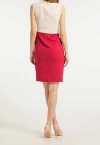 Robe ajustée avec un haut couleur crème et une jupe rouge. Tissu lisse ; longueur genou. Le dos présente une fermeture éclair discrète et des détails de couture minimaux.