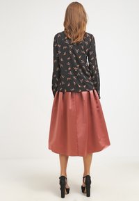 Svart blommig blus med långa ärmar, matchad med en glänsande satinfärgad rosaskjorta, som har en utsvängd design, samt svarta högklackade skor.